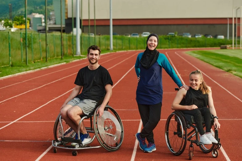 Two friends in wheelchairs with support worker on sports track