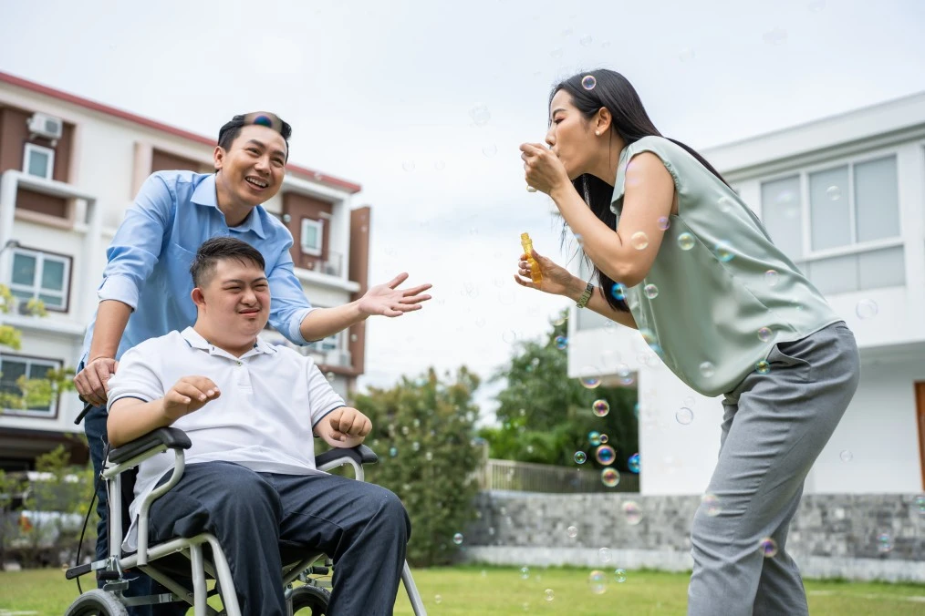 Disabled boy in wheelchair smiling with family outside blowing bubbles