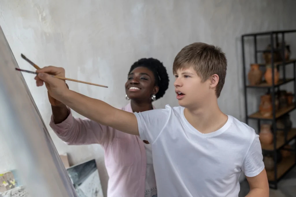 Boy with down syndrome painting with support worker